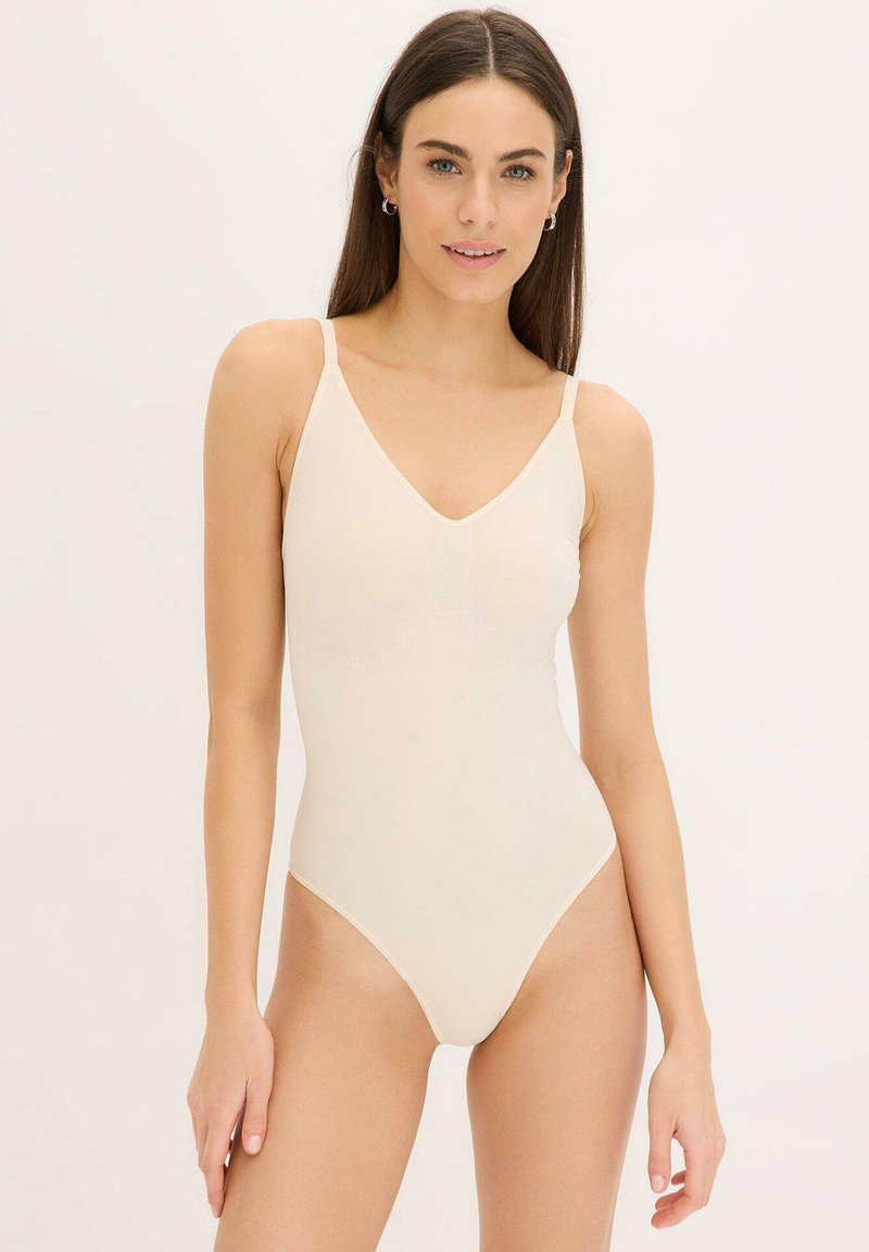 Costume da bagno intero beige con spalline sottili, scollatura a V e texture liscia, caratterizzato da un design minimalista e aperture delle gambe alte.