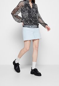 Schwarze, blumengemusterte durchsichtige Bluse mit langen Ärmeln, kombiniert mit einem hellen Jeans-Minirock. Schwarze Plateau-Schuhe runden das Outfit ab.