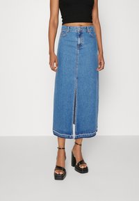 Denim-maksihame, jossa on edessä halkio, vaaleansininen väri, klassinen viisi-taskuinen muotoilu ja raaka helma. Yhdistetty mustiin hihna-sandaaleihin, joissa on avara korko.