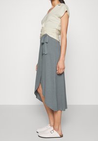 Light beige wrap top with short sleeves, paired with a loose, heathered gray asymmetrical skirt and white clogs. Smooth texture, casual design.