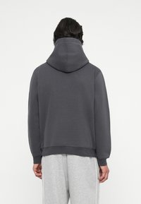 Sudadera gris oscura con una gran capucha, puños y dobladillo acanalados. Textura suave. Se lleva con pantalones de chándal gris claro que presentan rayas laterales.