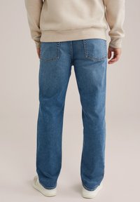 Gaiši zili džinsi ar brīvu piegriezumu, kuriem ir divas aizmugurējās kabatas un smalki izšuvumi. Audumam ir gluda tekstūra.