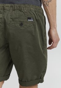 Shorts vert olive à coupe décontractée, dotés d'une taille élastique, de poches latérales, d'une poche arrière avec bouton et de poignets retournés.