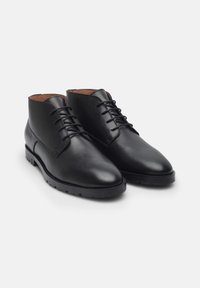 Bottines en cuir noir avec une texture lisse, pointe pointue, six œillets pour lacets et semelle en caoutchouc dotée de crampons pour une meilleure adhérence.