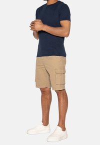 T-shirt en coton bleu marine et shorts cargo beiges avec poches latérales, associés à des baskets blanches. Les shorts présentent des détails cousus et une coupe décontractée.