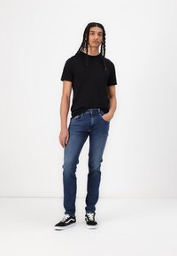 Fekete, rövid ujjú póló, kék, slim-fit farmernadrág és fekete sportcipő. A farmernadrág középmagas derékkal rendelkezik, az öltözet egyszerű és laza.