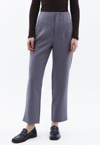 Grå skräddarsydda byxor med hög midja, vertikala sömmar och rak passform, kombinerade med svarta loafers. Slät tygtextur.