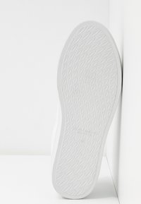 Hvit sneakersåle med et teksturert diamantmønster for grep, med en glatt kant og minimalistisk design.