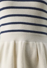 Robe en maille avec un corsage crème côtelé orné de rayures horizontales bleu marine ; jupe évasée à texture douce et détails plissés.