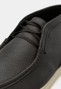 Καφέ δερμάτινο παπούτσι με υφή στην επιφάνεια, στρογγυλεμένη μύτη και κορδόνια. Διαθέτει ραφές σε αντίθετο χρώμα και σόλα σε κρεμ απόχρωση.