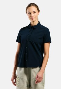 Navy short-sleeve shirt with button closure, chest pocket, and smooth texture. Features a curved hem and subtle branding on the lower side.