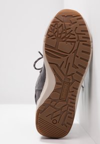 Baskets en daim gris avec une semelle en caoutchouc texturée ; elles présentent un motif de semelle extérieure marron, des lacets ronds et un logo sur un accent beige.