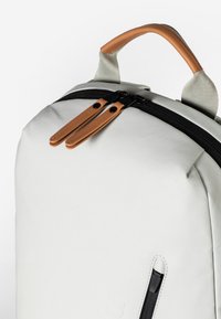 Weißer Rucksack mit glatter Oberfläche, schwarzem Reißverschluss, Ledergriffen und Akzentgurten. Kompaktes Design mit minimalistischem aesthetic.