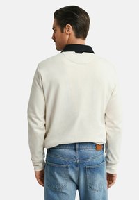 Polo blanc à manches longues avec col noir, associé à un jean en denim bleu clair. Le tissu semble lisse ; le col présente un accent contrastant.