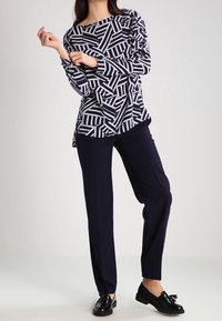 Marinblå och vit mönstrad långärmad topp med geometriska mönster, tillsammans med marinblå byxor och svarta slip-on skor. Platt, slät textur.