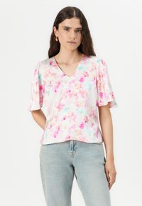 Blusa corta de manga corta con estampado floral en colores pastel y escote en forma de V, con una textura sedosa y mangas con volantes. Se combina con jeans de mezclilla claros.