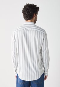 Gestreepte shirt in lichtgrijs en witte katoen, met een klassieke kraag, knoopmanchetten en een afgeronde zoom. De stof lijkt soepel en gestructureerd.