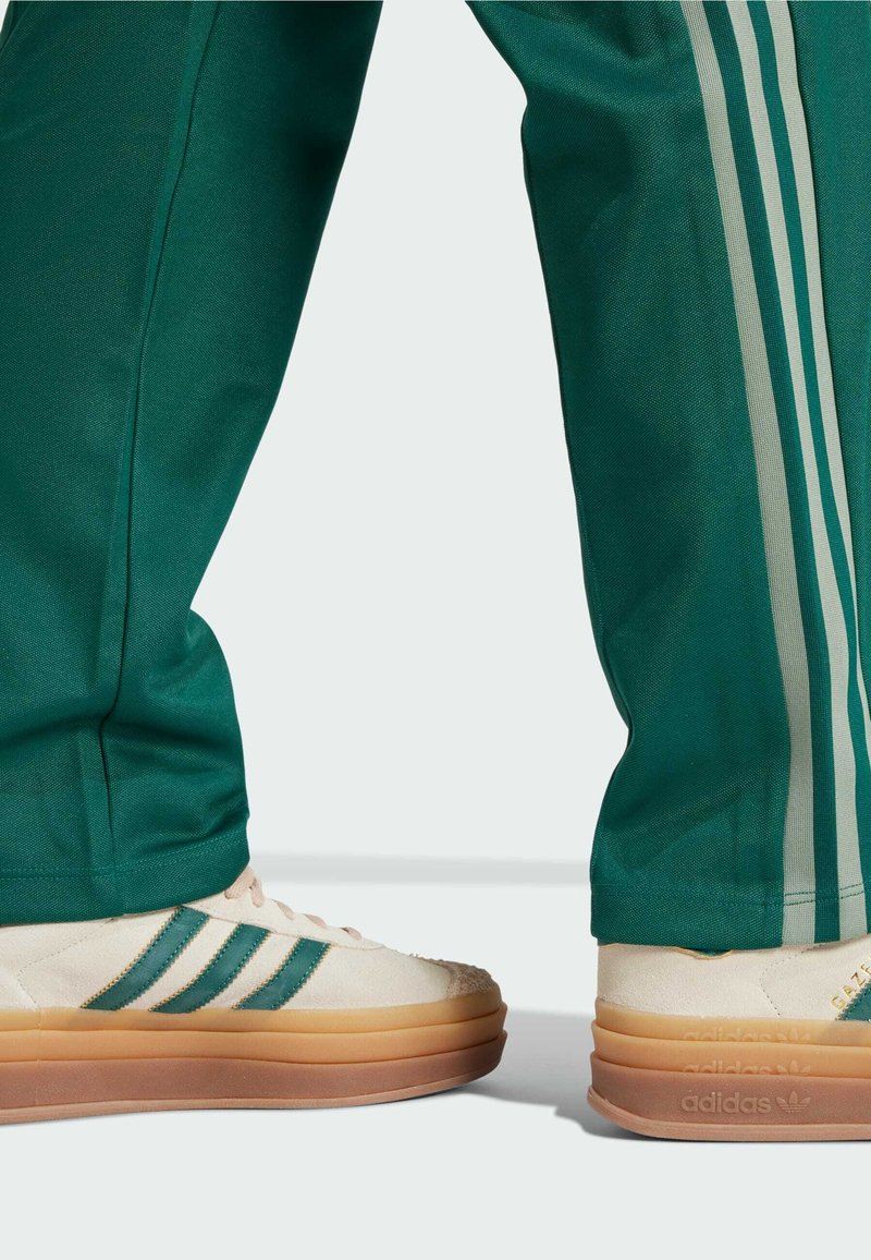 Zielone spodnie sportowe z trzema jasnolimonkowymi paskami; beżowe buty z zielonymi paskami, teksturowanym wierzchem i gumowymi podeszwami, z oznaczeniem marki.