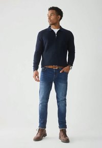 Maglione blu navy con zip, jeans blu, stivali in pelle marrone. Outfit casual con maglia strutturata, colletto e design a vestibilità slim.