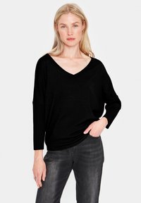 Svart V-ringad tröja med långa ärmar, tillverkad av ett texturerat tyg, kombinerad med mörkgrå jeans med en avslappnad passform.