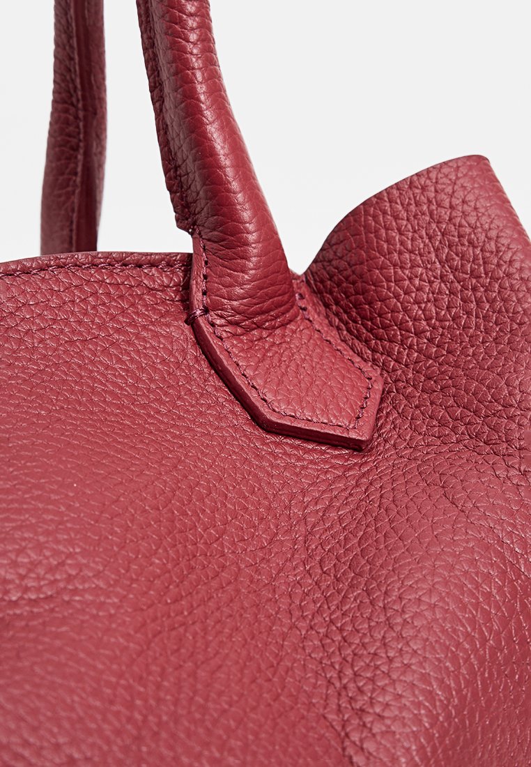 Borsa a mano strutturata in pelle rossa con superficie texturizzata, forma arrotondata e due manici robusti. Presenta un accento cucito vicino alla base.