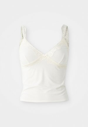 Camisola bianca realizzata in morbido tessuto con dettagli in pizzo sulle spalle e sul neckline. Presenta un taglio a V sul davanti e un fiocchetto decorativo al centro.