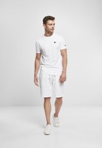 White cotton t-shirt with a small black logo, paired with white cotton shorts and white sneakers, minimalistic design, smooth texture.