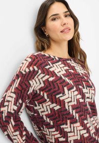 Maglione lavorato a maglia con un motivo a zigzag in tonalità bordeaux, crema e viola scuro. Texture morbida con colletto rotondo e maniche lunghe.