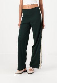 Wijdvallende broek in donkergroen stof met een crèmekleurige zijstreep. Platte tailleband met een gladde textuur, geschikt voor zowel casual als formele gelegenheden.