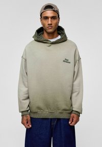 Grüne Gradient-Hoodie mit lässigem Schnitt, ausgestattet mit einer Fronttasche und dem Text "Stay Moment" in dunkelgrüner Stickerei auf der Brust.