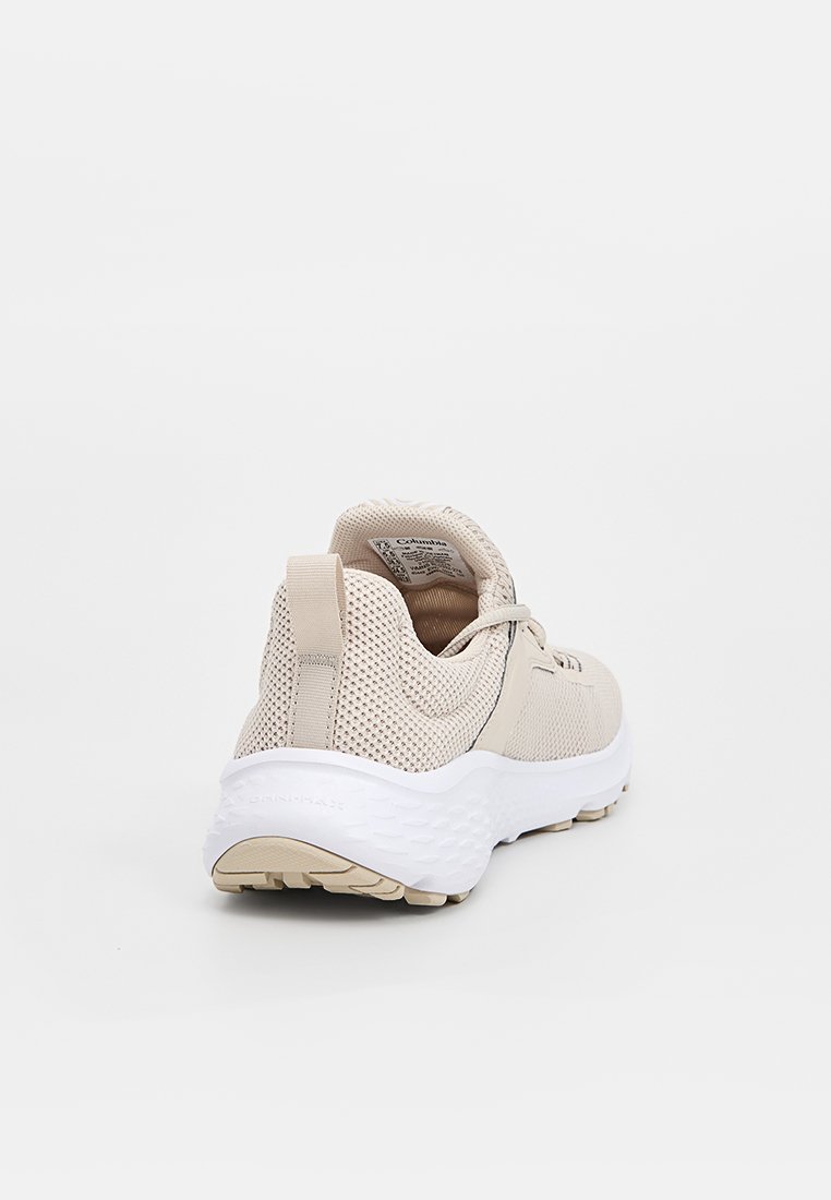 Zapatilla deportiva color beige con parte superior de malla, cuello acolchado y suela blanca. Incluye una lengüeta para facilitar el calzado y una suela texturizada para un mejor agarre.