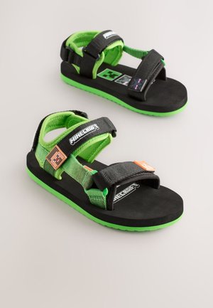 Schwarze und grüne Kindersandalen mit verstellbaren Riemen, einer profilierten Gummisohle, Logodetails und einem weichen, gepolsterten Innenfutter.