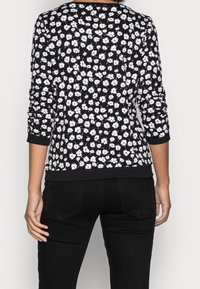Felpa nera con motivo floreale bianco e rosso, maniche lunghe e orlo e polsini a costine, indossata con jeans neri.