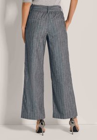 Wijde broek van grijze stof met subtiele verticale strepen, voorzien van achterzakken en een elastische tailleband, gecombineerd met hoge hakken.