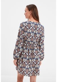 Langärmliges Kleid mit einem floralen Muster in Weiß, Marineblau, Rot und Orange. Hat eine geraffte Taille und einen runden Ausschnitt.