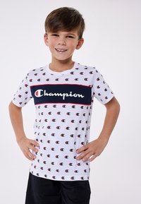 White cotton t-shirt with small repeating Champion logo patterns, featuring a navy blue central band with "Champion" text in white. Short sleeves.