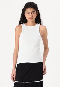 Débardeur blanc côtelé avec un col rond et sans manches. Associé à une jupe noire avec une bordure festonnée au bas.
