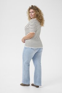 Camicia a maniche corte a righe bianche e nere, abbinata a jeans svasati celesti. Il modello è ritratto di profilo, mostrando l'outfit.