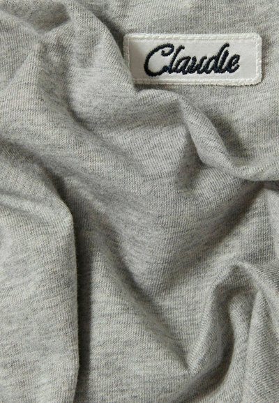 Tessuto di cotone grigio con una texture morbida, caratterizzato da un'etichetta bianca cucita con la scritta "Claudle" in carattere corsivo blu navy.