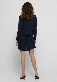 Blazer bleu marine avec un design ajusté et des manches longues, associé à une robe bleu marine en couches avec une jupe évasée et une texture transparente.