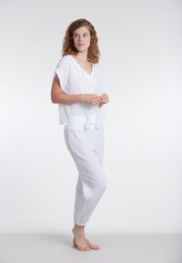 Valkoinen puuvillainen loungewear-setti, joka sisältää löysän V-kaula-aukollisen lyhythihaisen paidan ja istuvat, teksturoidut housut.