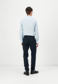 Hellblaues Langarmhemd mit Knöpfen, dunkelblaue Hose und schwarze Schuhe, von hinten auf einem schlichten weißen Hintergrund betrachtet.