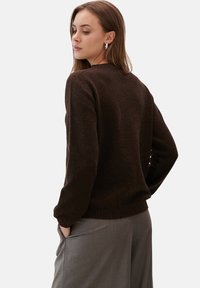 Brązowy sweter z dzianiny o okrągłym dekolcie i długich rękawach, z teksturowanym wykończeniem i prążkowanym dołem, zestawiony z szarymi spodniami.