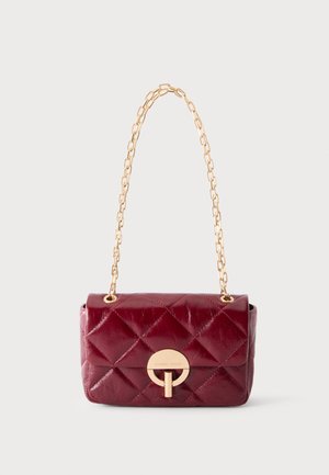 Petit sac à main en cuir rouge foncé matelassé avec fermoir circulaire doré et bandoulière chaîne dorée sur fond uni.