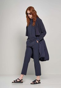 Tuta navy con vestibilità ampia, composto da una giacca corta e pantaloni a gamba dritta. Abbinato a sandali neri con cinturini e occhiali da sole.