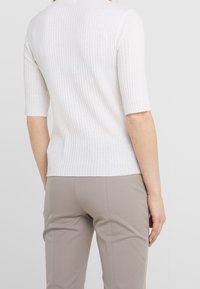 Biały prążkowany top z krótkimi rękawami, o dopasowanym kroju i subtelnej fakturze. Zestawiony z jasnobeżowymi spodniami slim fit.
