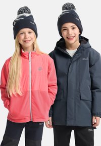 Zwei Kinder tragen Oberbekleidung: eine pinke Fleecejacke mit einem grauen Logo und eine dunkelgraue wasserfeste Jacke, beide kombiniert mit Mützen.