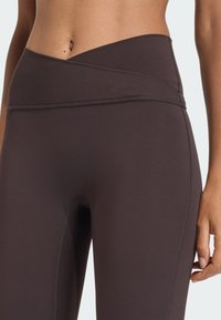 Leggings a vita alta, marrone scuro, caratterizzati da un design senza cuciture, texture morbida e un cinturino piegato con dettagli di cucitura sottili.