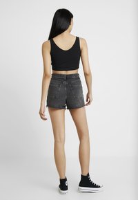 Svart kort topp med bred ryggöppning, kombinerad med högmidjade, slitna svarta denimshorts. Stylad med svarta högskaftade sneakers.