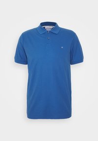 Polo bleu en coton lisse. Il présente un col avec deux boutons, des manches courtes et un petit logo sur la poitrine.